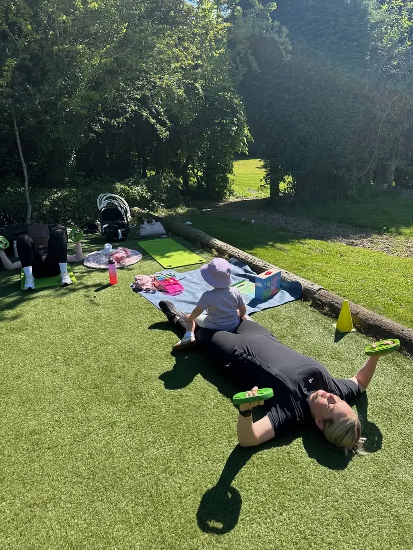 Mums training outdoors on the astro turf with their young children playing on a blanket beside them