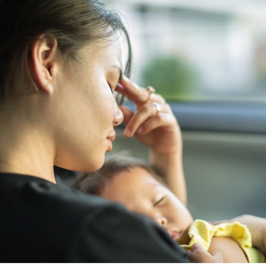 A tired mother resting her head on her hand while holding her sleeping baby