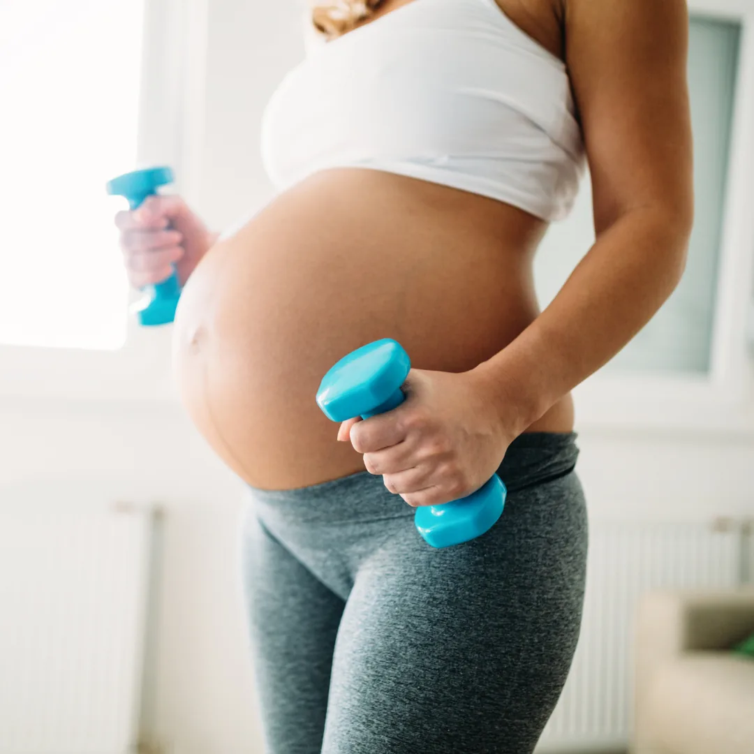A pregnant woman holding a pair of small dumbbells during a workout at home