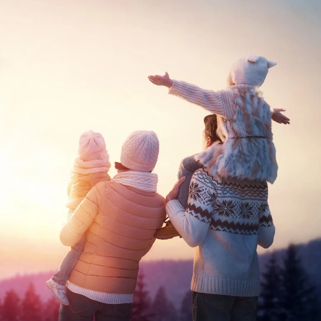 A family wrapped up in winter clothes watching the sunset together, parents carrying their two young children